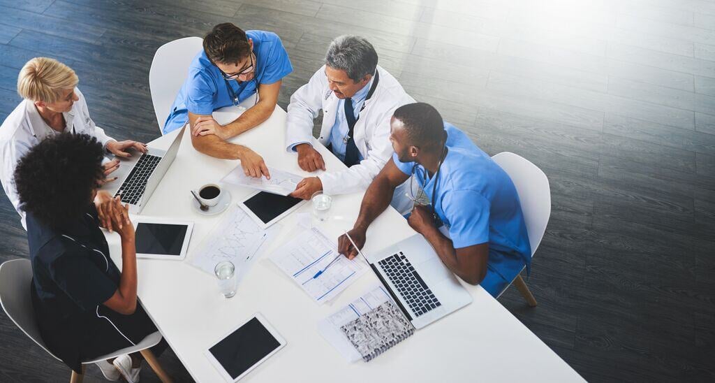 2435_Team of healthcare workers meeting with laptops around table